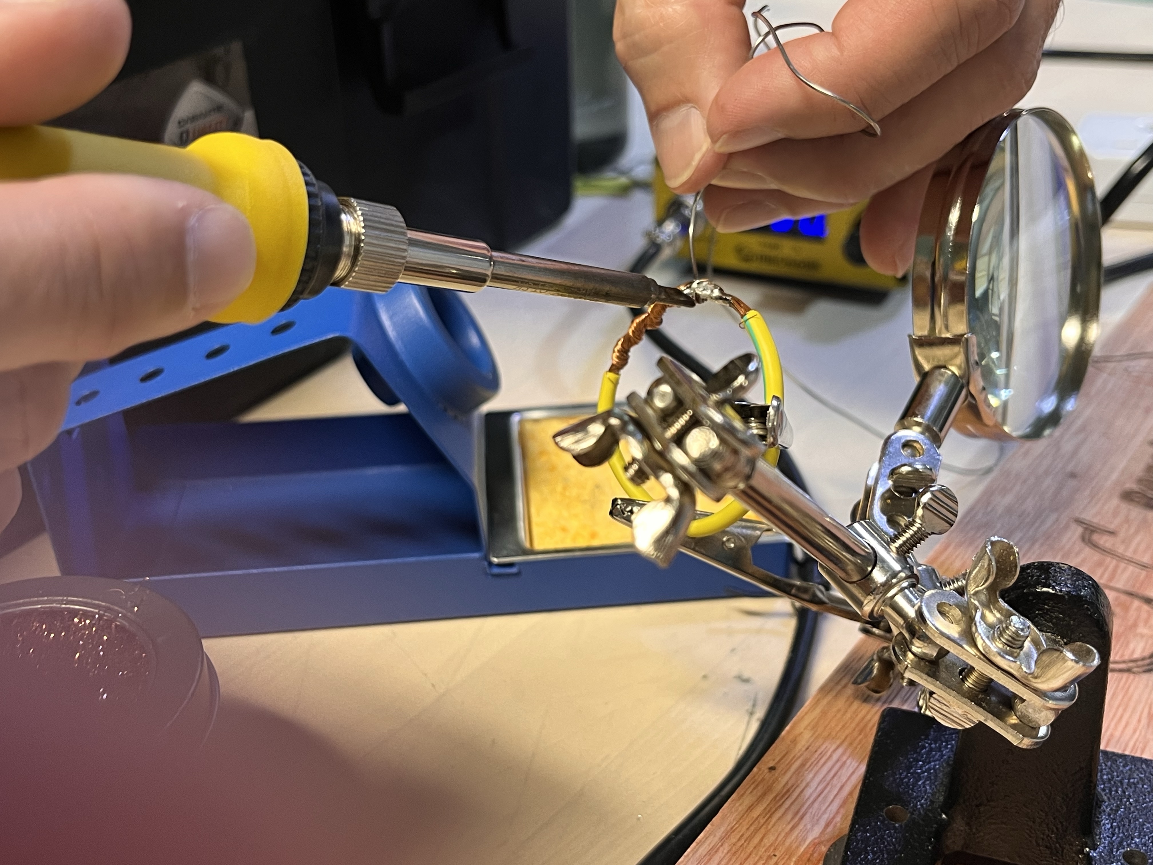 wires being soldered with help of a soldering iron and a helping hands apparatus